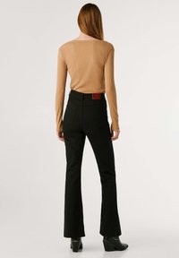 Top marrón de manga larga acanalado combinado con jeans flared negros de cintura alta, que presenta un parche en la parte posterior y bolsillos traseros. Calzado en negro.