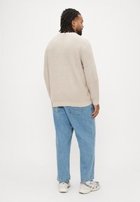 Maglione beige lavorato a maglia con vestibilità comoda, abbinato a jeans larghi azzurri chiari e sneakers grigie, visto da dietro.