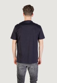 T-shirt in cotone blu navy scuro con maniche corte e scollatura a giro, mostrato dal retro, abbinato a jeans grigi scoloriti.