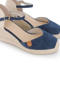 Sandalias de cuña de ante azul marino con suelas de yute trenzado, que presentan una correa de tobillo con hebilla dorada y un respaldo abierto texturizado.