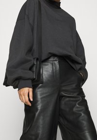 Överdimensionerad mörkgrå sweatshirt med långa ärmar, kombinerad med högmidjade svarta läderbyxor. Inkluderar en svart axelremsväska.