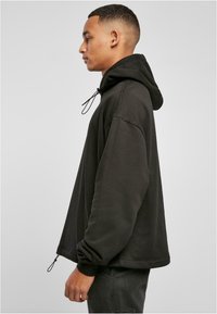 Sudadera negra con un corte relajado, cordón ajustable, puños acanalados y dobladillo. Hecha de una tela suave con una textura lisa.