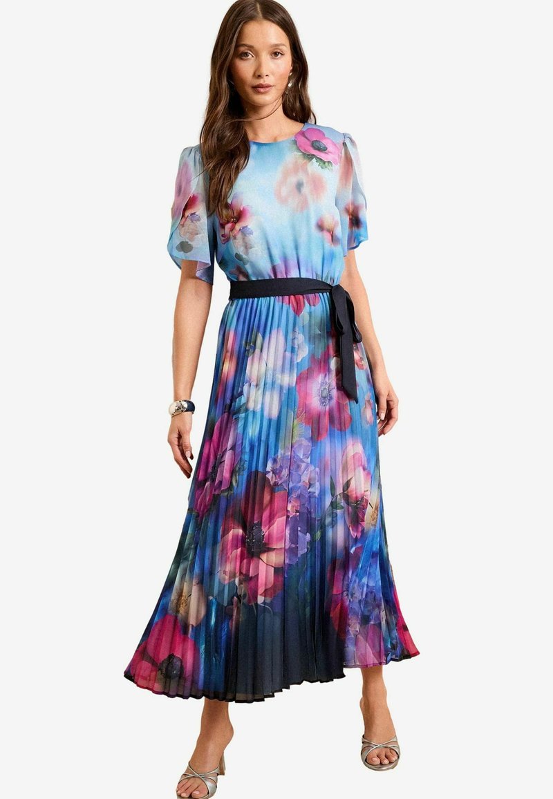 Ránc pleno maxi ruha virágmintával, kék, rózsaszín és lila árnyalatokban. Rövid ujjú és fekete derékrész részlettel. Könnyű, áramló anyag.