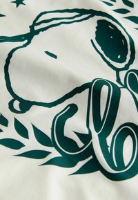Katoen stof met een groene illustratie van een hondenhoofd, omringd door gestileerde bladeren en decoratieve tekst op een crèmekleurige achtergrond.