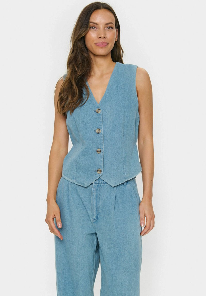 Svetlo modra traperjacket z V-izrezom, brez rokavov in petimi kovinskimi gumbi spredaj. Gladka tekstura in natančen kroj.