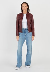 Bordeaux leren motorjack met gewatteerde schouderdetails, gecombineerd met lichtblauwe wijde jeans en witte sneakers.