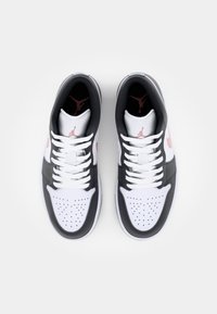 Pár bílých a černých tenisek s růžovým znakem Nike a logem Jumpman na jazycích a insoles, pohled shora na bílém pozadí.