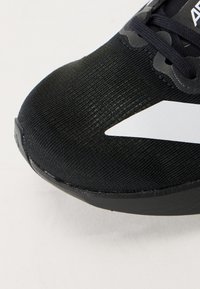 Chaussure de sport noire avec une tige en tissu texturé et une semelle lisse noire. Présente un logo blanc et des lacets noirs plats.