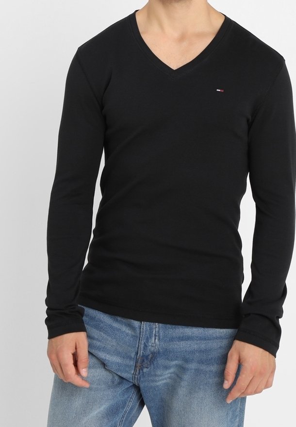 Schwarz langärmliges V-Ausschnitt-Shirt aus weichem Material, mit einem kleinen Logo im Brustbereich, kombiniert mit hellblauen Jeans.