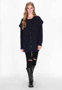 Granatowy sweter nabrzeżny z guzikami z przodu, szerokimi rękawami i fakturowanym materiałem; połączony z czarnymi dżinsami z dziurami i czarnymi kozakami za kolano.