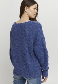 Pull en tricot bleu avec une coupe ample, un col large et des poignets côtelés. Texture douce avec une apparence confortable.