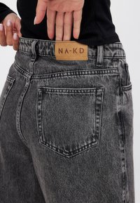 Svarta högmidjade jeans med en urtvättad design, som har en brun läderlapp med "NA-KD" på baksidan av midjan och standard bakfickor.