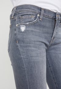 Modré džíny z denimu s vybledlým povrchem, opotřebovanými detaily, pěti kapsami a kontrastním prošíváním na pase.