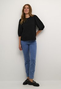Top negro texturizado con mangas abullonadas, combinado con jeans rectos azul claro y mocasines negros con acentos de hardware dorado.