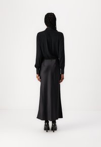 Svart langermet bluse med krage, kombinert med et elegant svart sateng maxiskjørt, med elastisk midje og glatt tekstur.