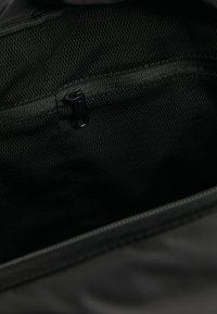 Svart väska inuti med en ficka med dragkedja, detaljer av nätmaterial och en slät struktur, designad för förvaring och organisering.