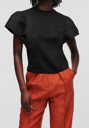 Czarny top z krótkim rękawem z bufkami na ramionach i okrągłym dekoltem, zestawiony z pomarańczowymi, teksturowanymi spodniami z wysokim stanem.