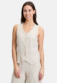 Gilet en lin beige avec des rayures blanches verticales, décolleté en V, boutons sur le devant et poches latérales, associé à un pantalon large assorti.
