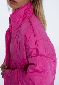 Helle pinke, gesteppten Jacke mit hohem Kragen und Reißverschluss. Verfügt über geschwungene Nahtmuster, gepolsterte Textur und eine lockere Passform.