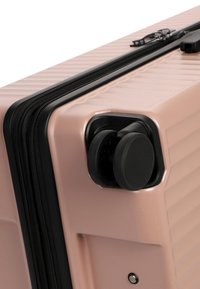 Valigia rigida rosa pallido con angolo e doppia ruota nera girevole, e dettagli zip neri lungo il bordo.