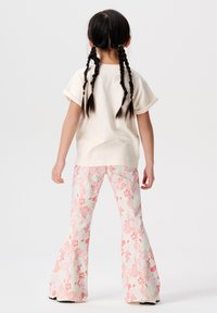 Beige t-shirt met korte mouwen en witte flared broek met roze koraalachtige bloempatronen. Het materiaal lijkt zacht en heeft een relaxte pasvorm.