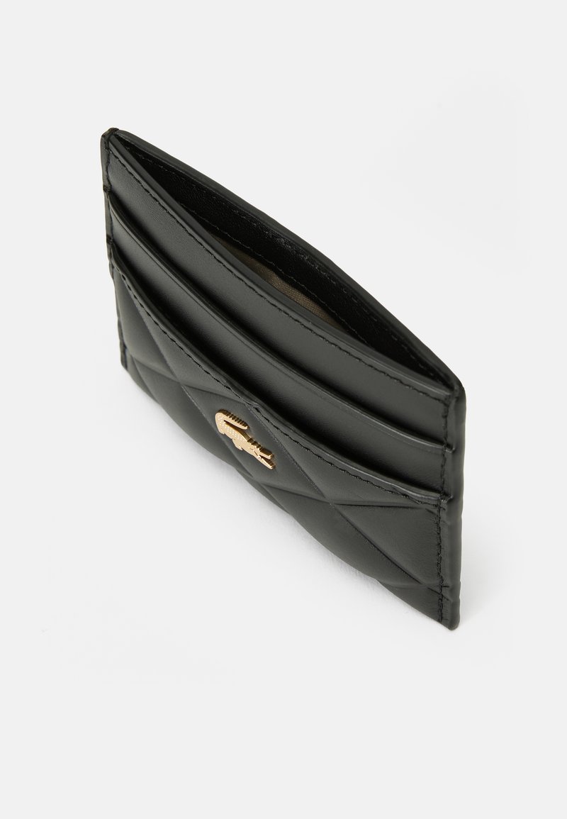 Porte-cartes en cuir noir matelassé avec logo crocodile doré, plusieurs emplacements pour cartes et compartiment central ouvert sur fond blanc.
