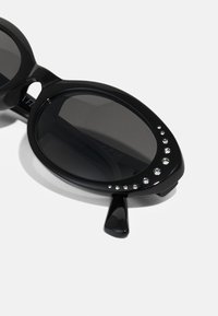 Black sunglasses with oval lenses and a glossy finish. Features a row of small rhinestones on the upper frame for embellishment.