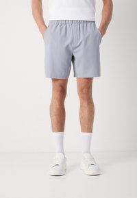 Grå svømmebukser med elastisk talje og sidelommer, kombinert med hvite sokker og joggesko, vist på en nøytral bakgrunn.