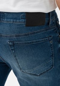 Vaqueros de mezclilla azul oscuro con un parche de cuero negro Hi-Flex en la cintura, diseño clásico de cinco bolsillos y detalles sutiles de costura.