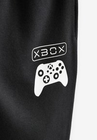 Schwarzer Stoff mit weißem Xbox-Logo und Grafik eines Gamecontrollers. Mit glatter Textur und klaren Linien, die das Branding hervorheben.