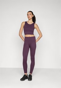 Lila bordázott crop top és hozzáillő, magas derekú leggings, rugalmas anyagból készült. Az öltözet fekete sportcipővel párosítva.