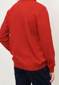 Rode gebreide trui met lange mouwen, geribbelde manchetten en zoom, met een eenvoudig ontwerp zonder patronen of versieringen.
