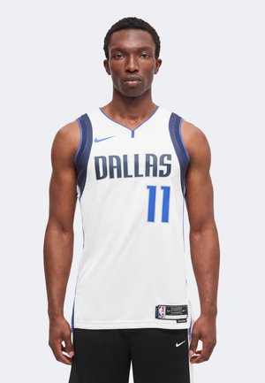 Jeune homme debout, portant un maillot de basket-ball blanc de Dallas avec le numéro 11 et un short noir avec un logo Nike.