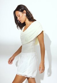 Haut drapé jaune clair avec une silhouette ajustée et des manches courtes, associé à un short blanc avec une délicate bordure en dentelle.