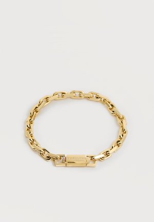 Bracelet chaîne doré avec fermoir rectangulaire gravé "HILFIGER" et petit détail de rayures rouges, blanches et bleues.