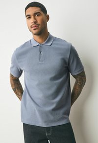 Ljusblå kortärmad polo med en vävd struktur, knäppning fram och ribbad krage. Kombinerad med mörka jeans.