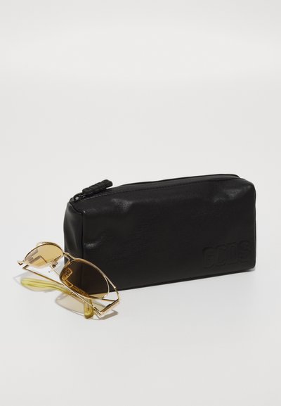 Black leather zipper pouch with embossed logo and textured finish, alongside gold-framed sunglasses with brown lenses and yellow tips.
