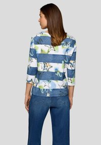 Mehrfarbiges Oberteil mit blauen und weißen Streifen, das ein Sternenmuster zeigt. Dreiviertelärmel und eine lässige, lockere Passform. Jeans in Denim-Blau.