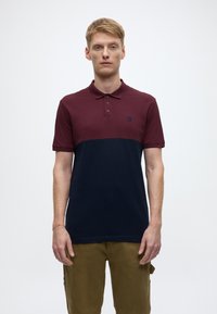 Burgundy and navy color-blocked polo shirt with three buttons, short sleeves, and an embroidered logo on the chest. Cotton blend fabric.