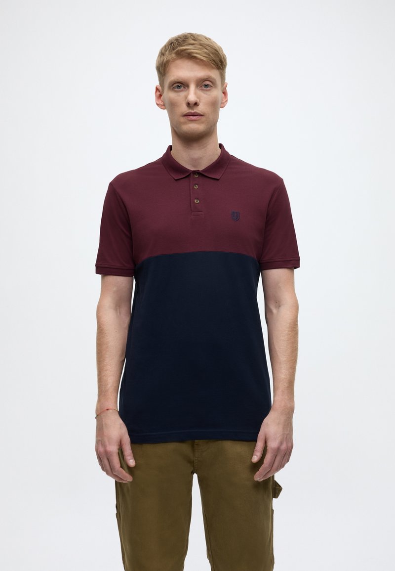 Burgundy and navy color-blocked polo shirt with three buttons, short sleeves, and an embroidered logo on the chest. Cotton blend fabric.