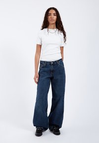 Vit kortärmad skjorta och mörkblå vida jeans. Skjortan har en figursydd design, jeansen har klassisk femficksstil och en lätt tvätt.