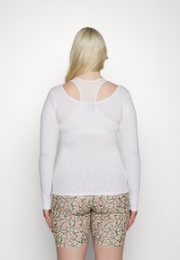 Top branco de manga longa com um design ajustado, apresentando um estilo de costas de nadador. Combinado com calções de flores, até à metade da coxa, em rosa e verde.