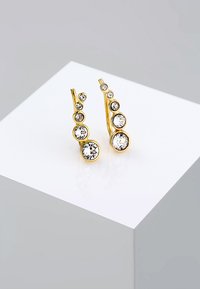 Øreringe i guldfarve med flere klare krystaller i forskellige størrelser, der har et buet design og en glat, poleret overflade.