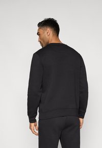 Melns džemperis ar apaļu izgriezumu un ribotu aproci. Gluds tekstūra, minimāls dizains ar taisnu apakšu, bez redzamiem logotipiem vai dizainiem.