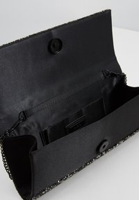 Svart kuvertväska med kedjedetaljer. Slät satininteriör och framsida, med ett enkelt knappstängning och en dragkedjeficka.
