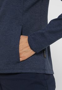 Námořnický modrý top s dlouh ým rukávem vyrobený z texturované látky, s bočními kapsami a logem na lemu. Čisté, rovné švy.