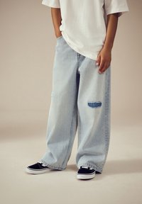 Lyseblå oversized jeans med revnet detalje og løs pasform, kombineret med sorte sneakers med hvide accenter. Ensfarvet hvid t-shirt.