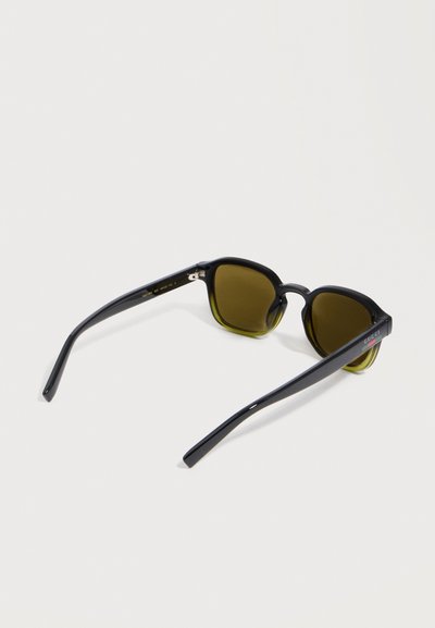 Lunettes de soleil à monture noire avec verres jaunes foncés et logo Gucci sur la branche, présentées en vue arrière trois-quarts sur fond blanc.
