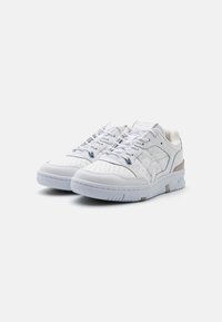Hvite lær sneakers med perforerte tær, snøring, lysegrå detaljer, teksturert hvit gummisåle og subtil merking på tungen.