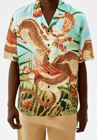 Košile s krátkým rukávem zdobená potiskem draka v živých barvách, především tyrkysové, oranžové a béžové, s volnějším střihem a zapínáním na knoflíky.